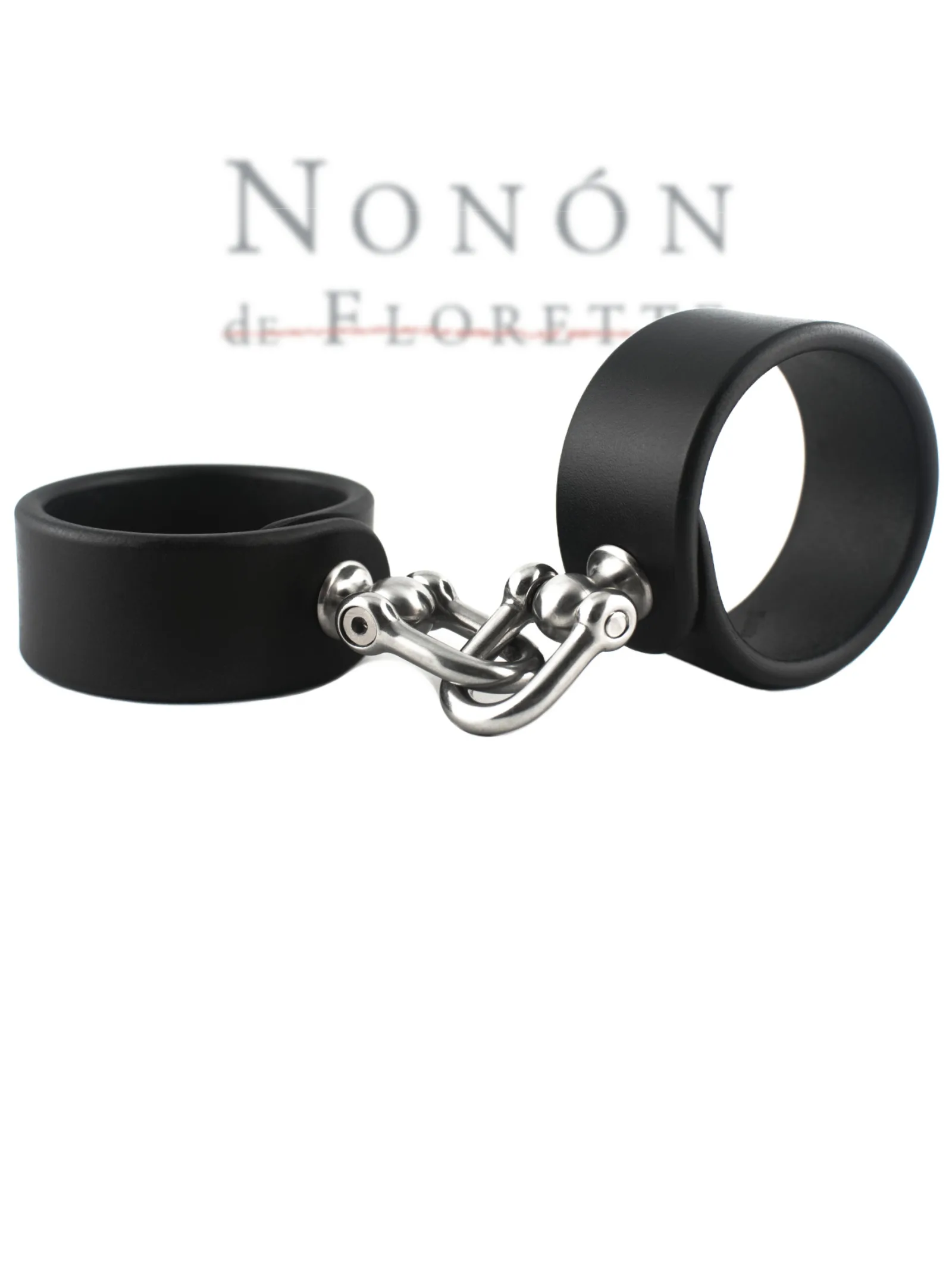pair of wide black leather cuffs by NoNón restrained with solid articulated metal shackles, photographed against a white background.